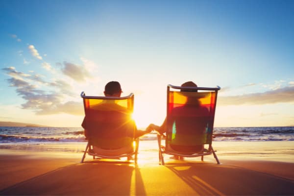 Couple sitting at water's edge in beach chairs holding hands